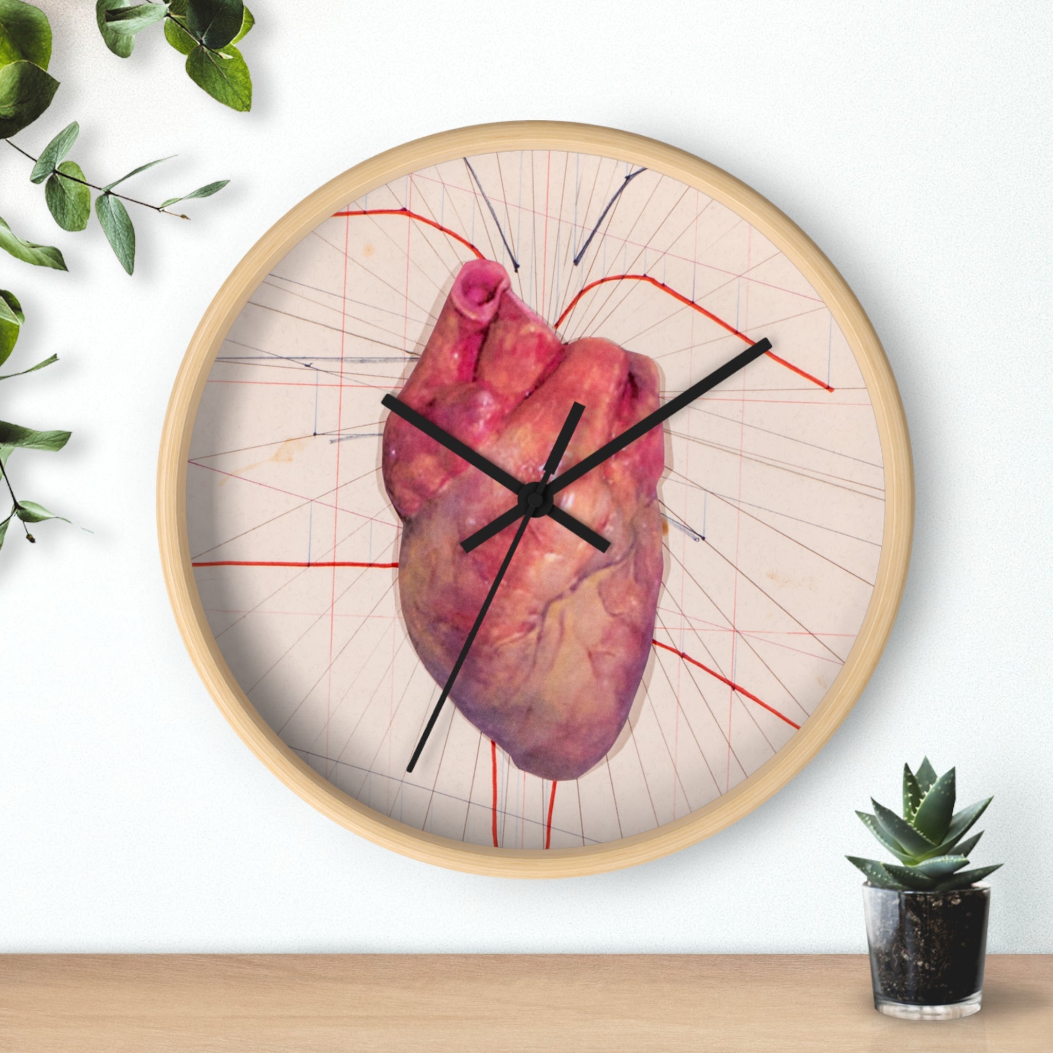 Round designer wall clock with anatomical heart illustration in red on a light background, black clock hands, and a natural wood frame, displayed on a wall.