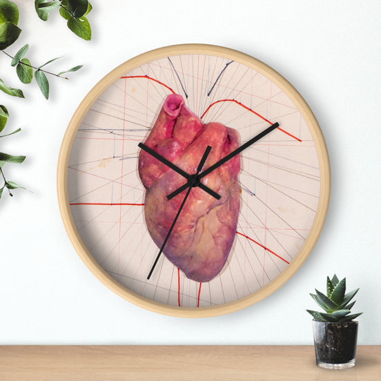 Round designer wall clock with anatomical heart illustration in red on a light background, black clock hands, and a natural wood frame, displayed on a wall.
